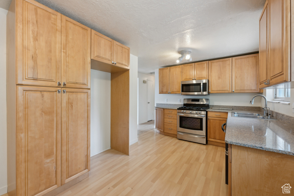 Kitchen with appliances with stainless steel finishes, a sink, light wood finished floors, and light stone countertops