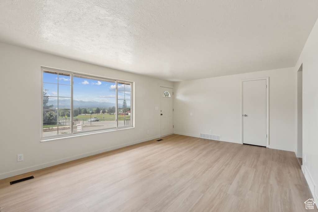 Empty room featuring light wood-type flooring, baseboards, and a textured ceiling