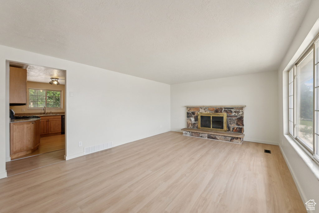 Unfurnished living room featuring a sink, light wood-style floors, a fireplace, and baseboards