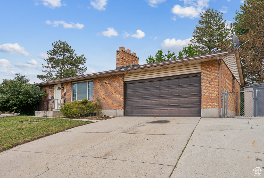 Ranch-style house with brick siding, concrete driveway, a chimney, and an attached garage