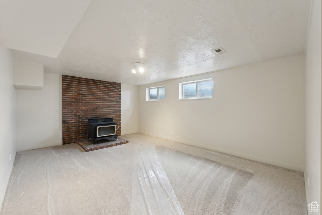Unfurnished living room featuring carpet, a wood stove, and baseboards