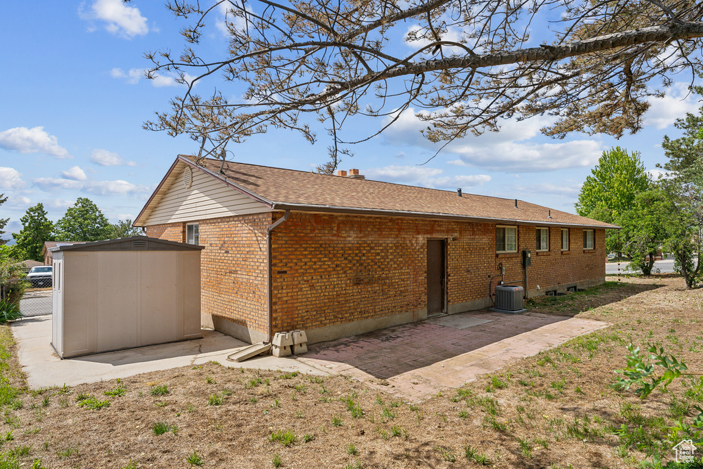 Back of property featuring brick siding, a patio area, central AC unit, and a chimney