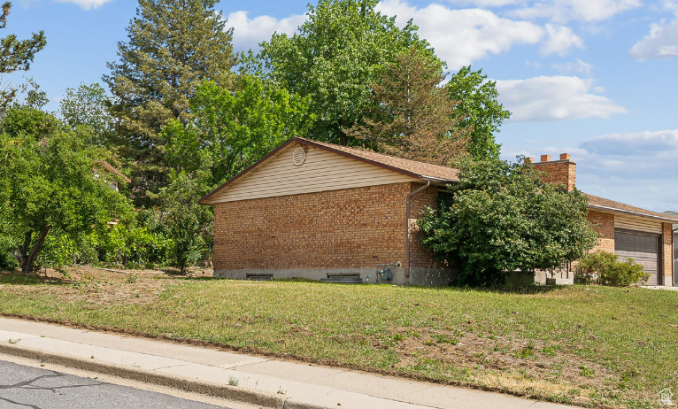 View of property exterior with brick siding, a garage, and a lawn