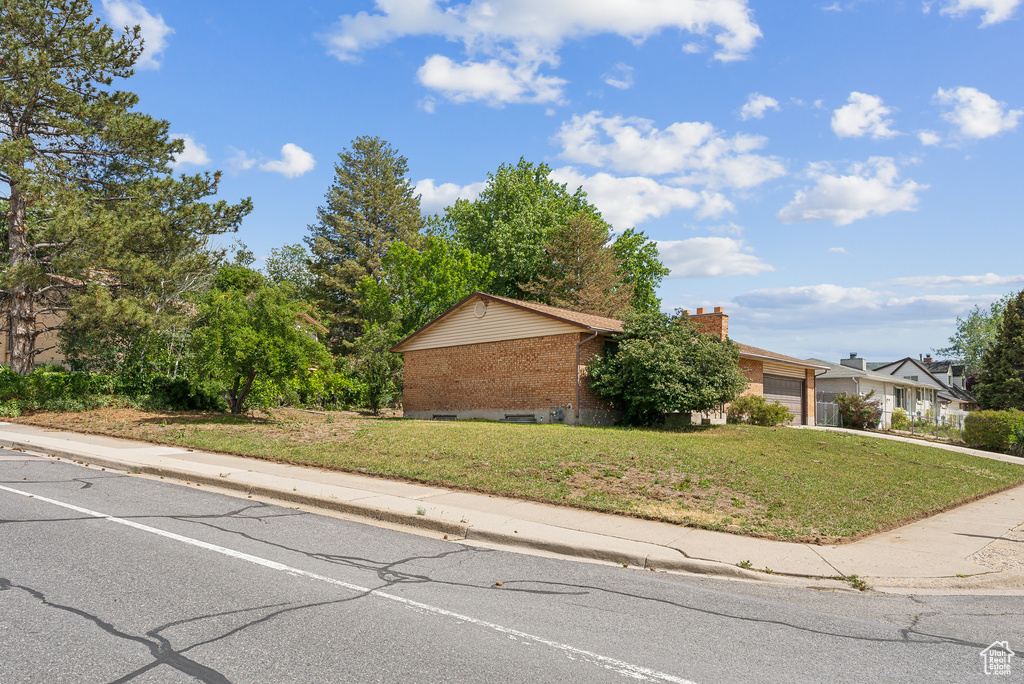 View of front of property featuring an attached garage, a front yard, brick siding, driveway, and a chimney
