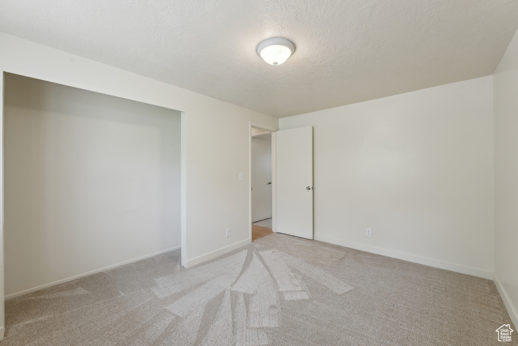 Unfurnished room with light carpet, a textured ceiling, and baseboards