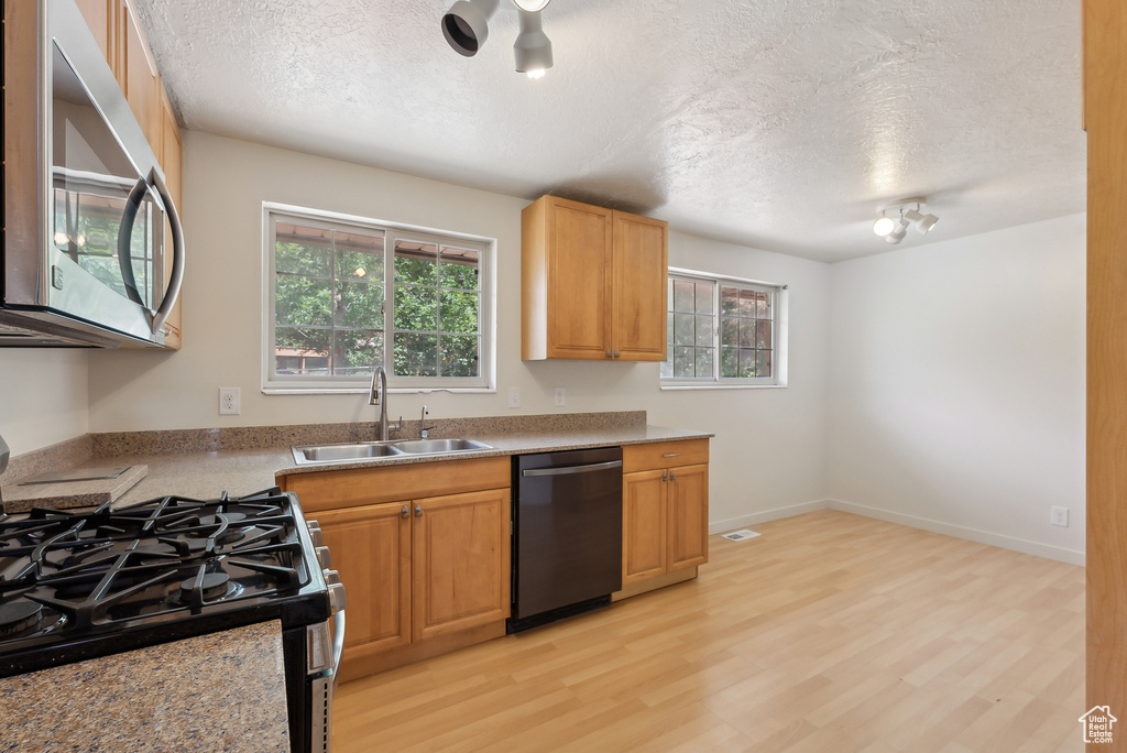 Kitchen featuring appliances with stainless steel finishes, a sink, a textured ceiling, healthy amount of natural light, and light wood-type flooring
