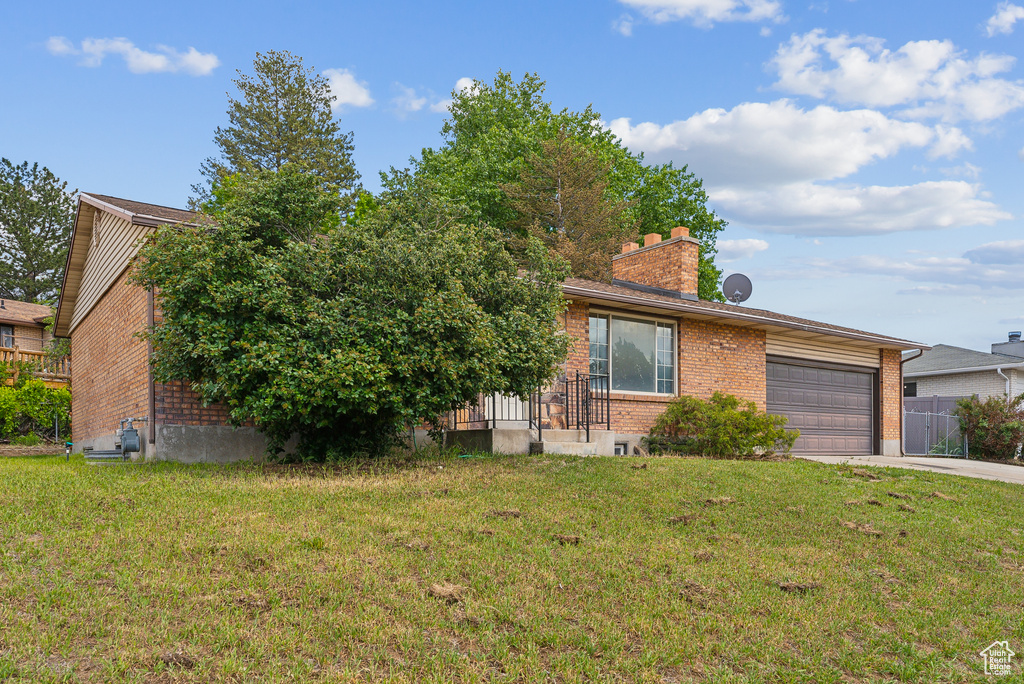 View of front of house featuring driveway, brick siding, a garage, a front lawn, and a chimney