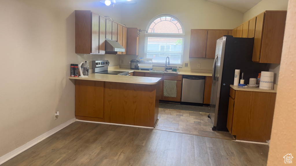 Kitchen featuring appliances with stainless steel finishes, under cabinet range hood, a sink, a peninsula, and lofted ceiling
