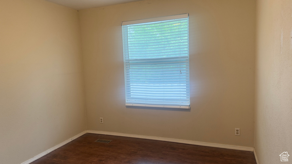 Empty room with dark wood-style floors, healthy amount of natural light, and baseboards