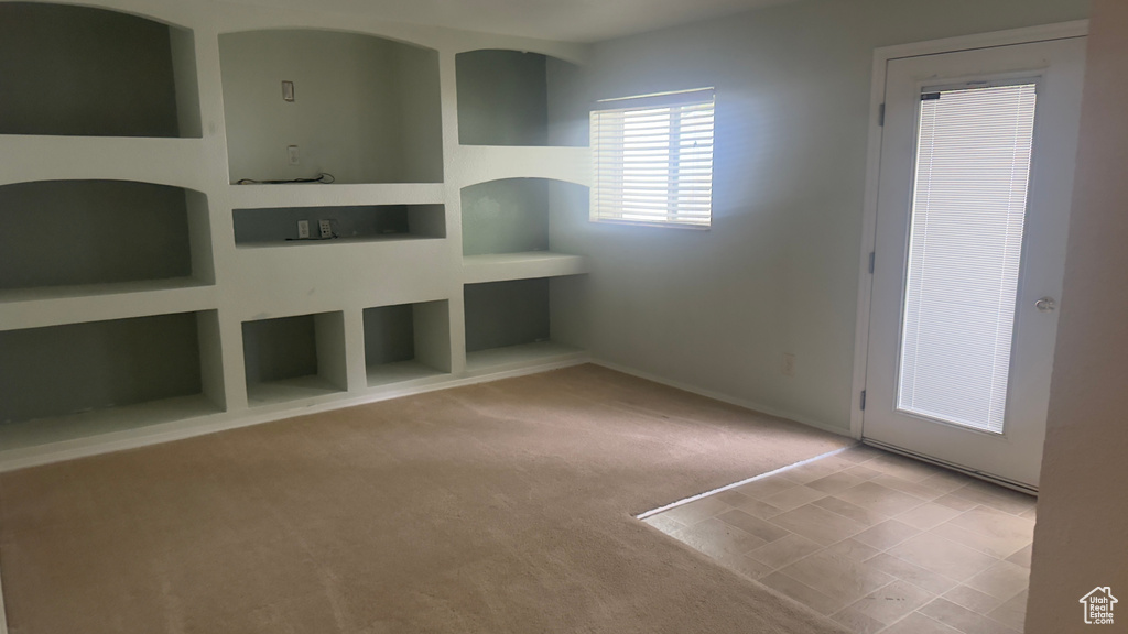 Unfurnished living room featuring built in shelves and carpet