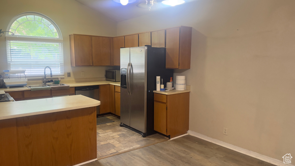Kitchen with a sink, stainless steel appliances, lofted ceiling, light countertops, and brown cabinets