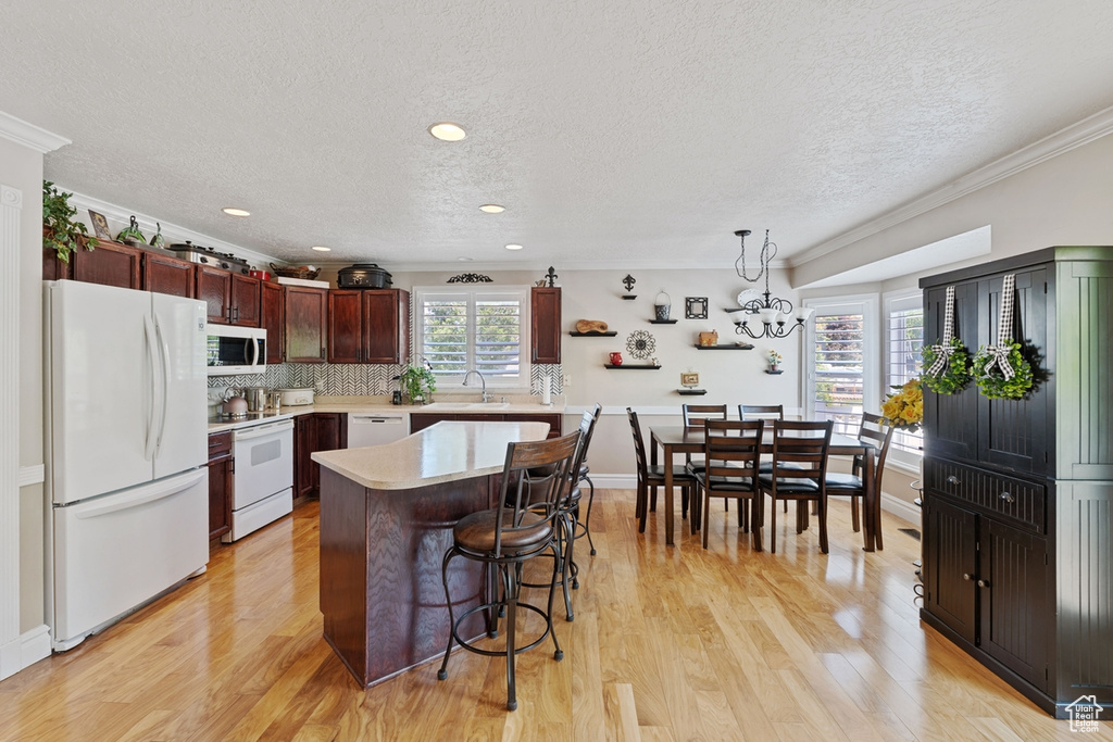 Kitchen with white appliances, light countertops, a textured ceiling, a breakfast bar area, and light wood-style floors