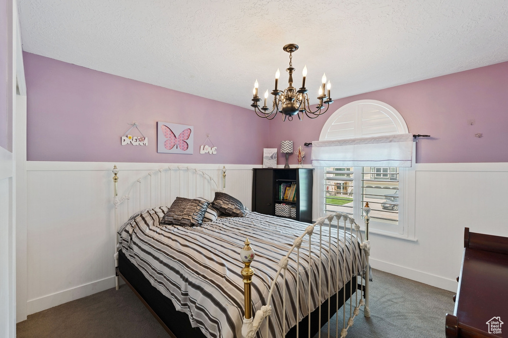 Bedroom featuring a chandelier, carpet, a wainscoted wall, a textured ceiling, and baseboards