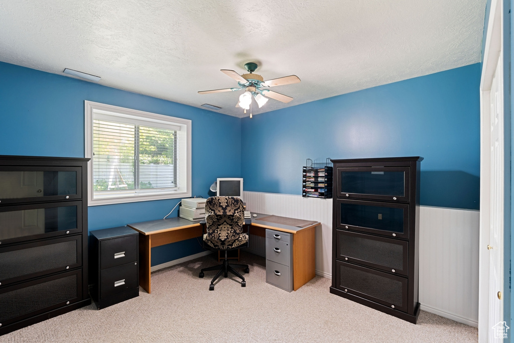 Office space with a ceiling fan, light colored carpet, a wainscoted wall, and a textured ceiling