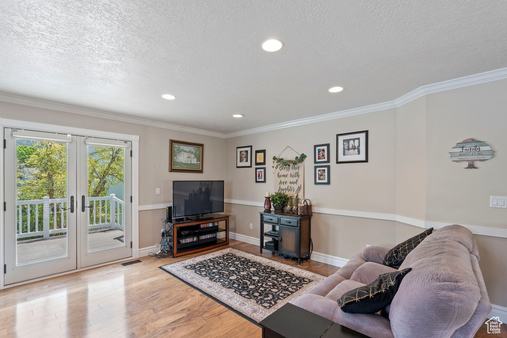 Living room with light wood finished floors, a textured ceiling, french doors, recessed lighting, and crown molding