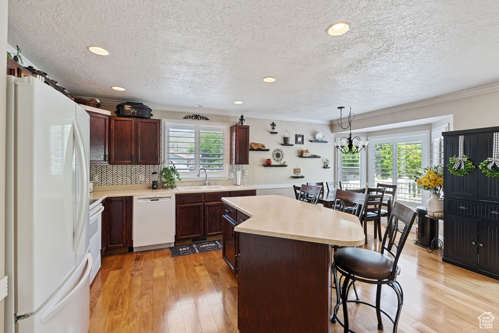 Kitchen with white appliances, a sink, a kitchen island, a kitchen bar, and ornamental molding