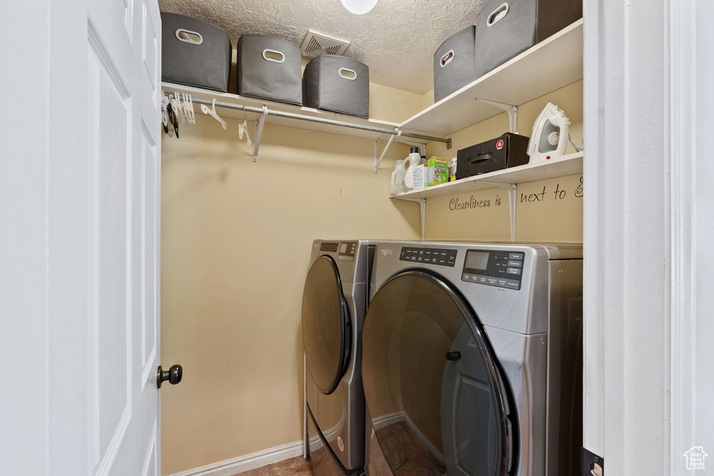 Washroom featuring washing machine and clothes dryer, a textured ceiling, and baseboards