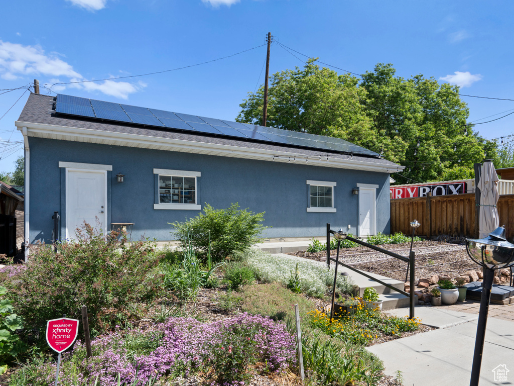 View of side of property with roof mounted solar panels, a vegetable garden, stucco siding, and roof with shingles