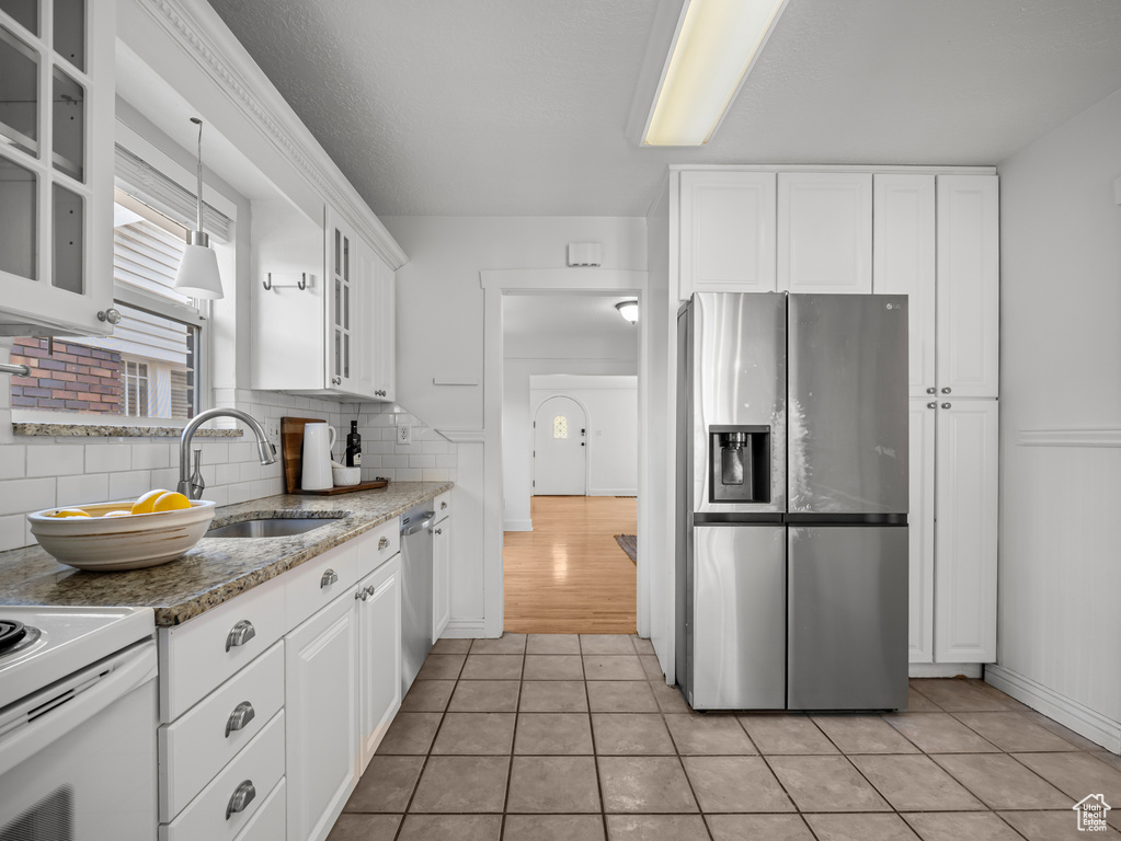 Kitchen with appliances with stainless steel finishes, white cabinets, tasteful backsplash, and glass insert cabinets
