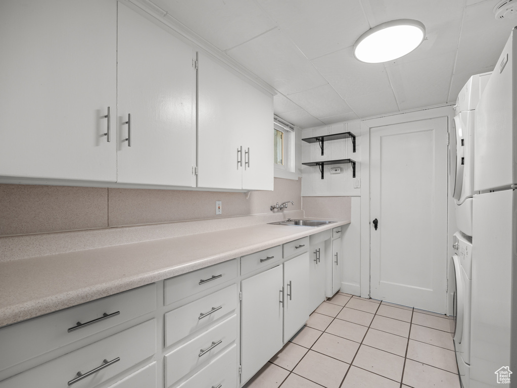 Kitchen with stacked washer and clothes dryer, light tile patterned floors, light countertops, and white cabinetry