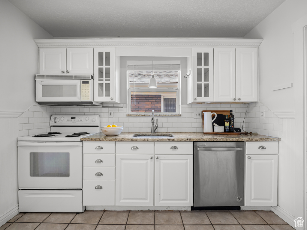 Kitchen featuring white appliances, white cabinetry, light tile patterned floors, glass insert cabinets, and tasteful backsplash