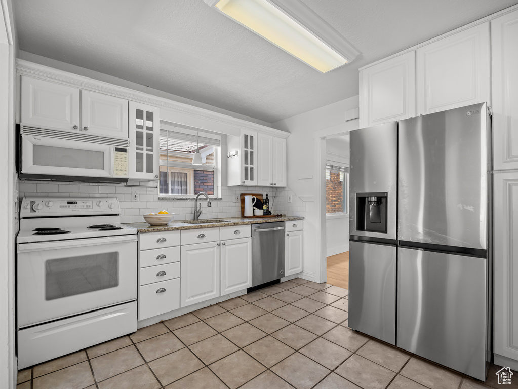 Kitchen with stainless steel appliances, white cabinets, glass insert cabinets, backsplash, and light tile patterned floors