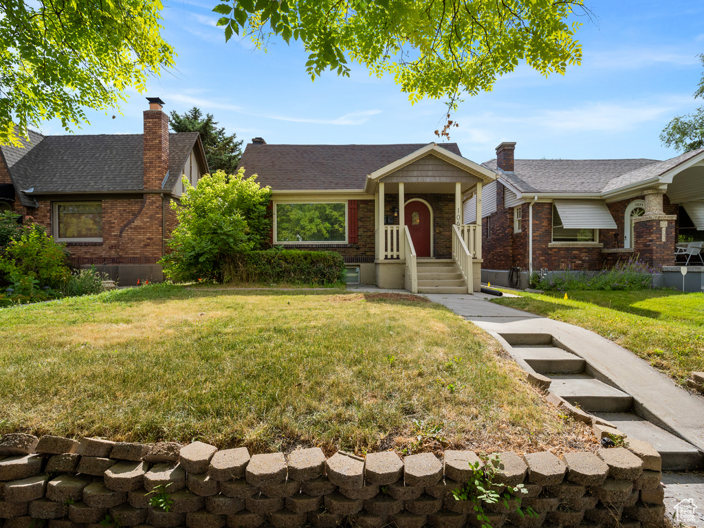 View of front facade featuring brick siding, a front yard, a chimney, and roof with shingles