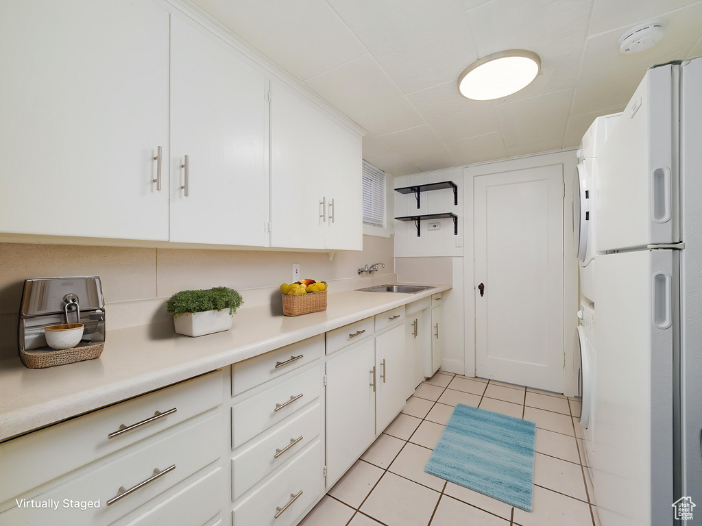 Kitchen with freestanding refrigerator, a sink, light tile patterned flooring, and white cabinets
