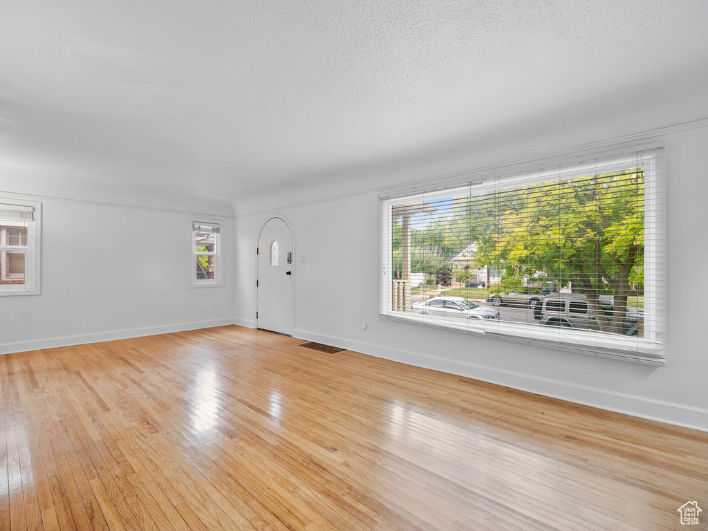Unfurnished living room featuring light wood-type flooring, baseboards, and a textured ceiling