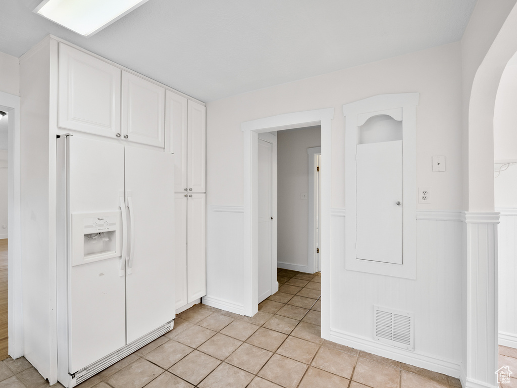 Kitchen featuring white fridge with ice dispenser, white cabinets, arched walkways, wainscoting, and light tile patterned floors