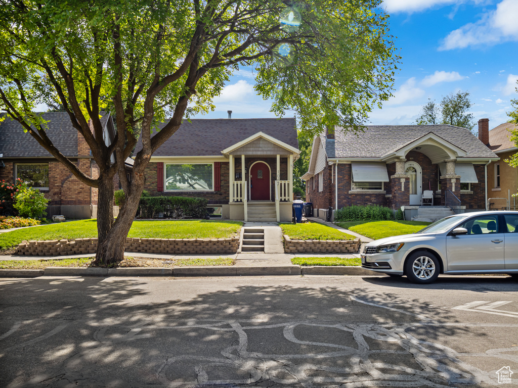 View of front facade with brick siding, a front yard, and a shingled roof