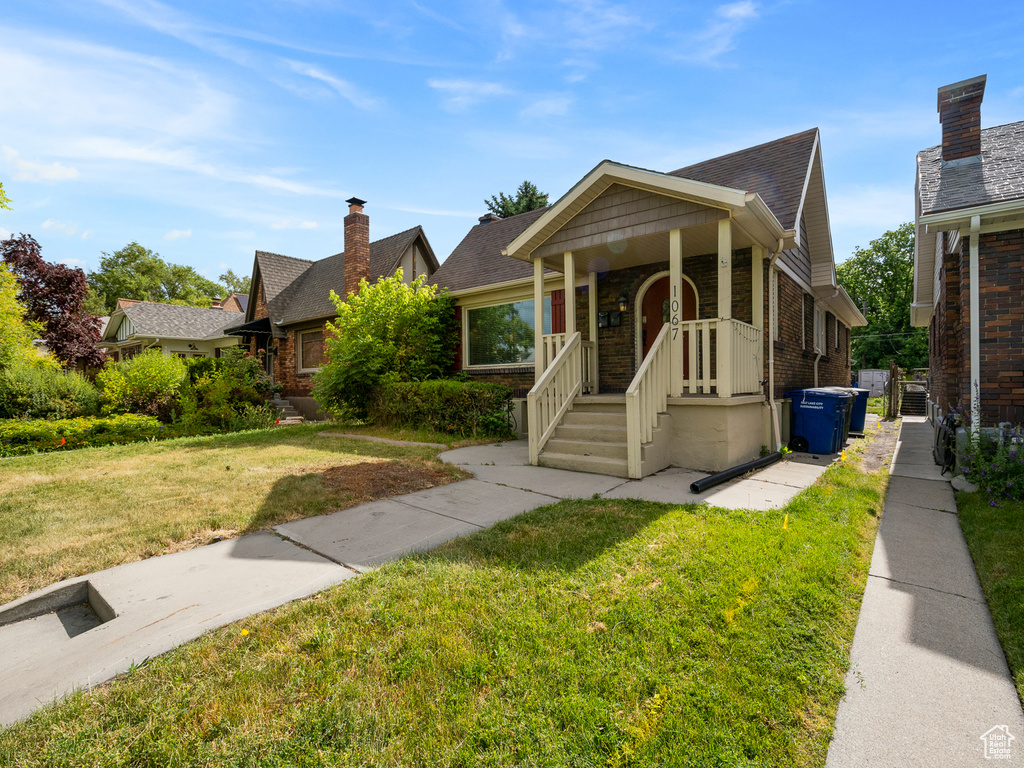 Bungalow-style home featuring a front lawn, brick siding, a chimney, and a shingled roof