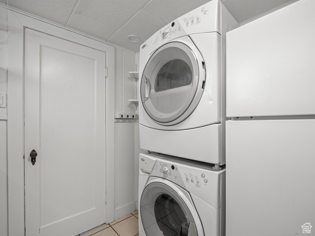 Washroom with stacked washer and clothes dryer and light tile patterned floors