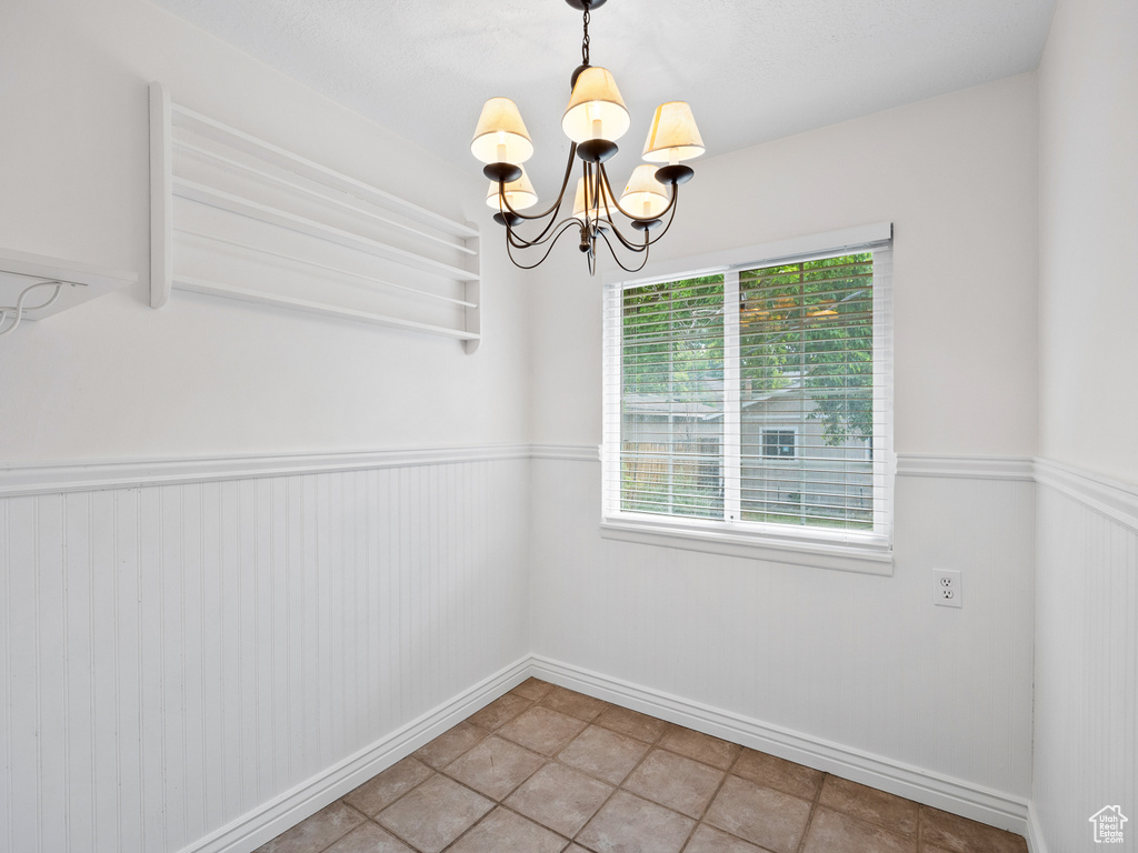 Unfurnished dining area featuring plenty of natural light, a chandelier, wainscoting, baseboards, and light tile patterned floors