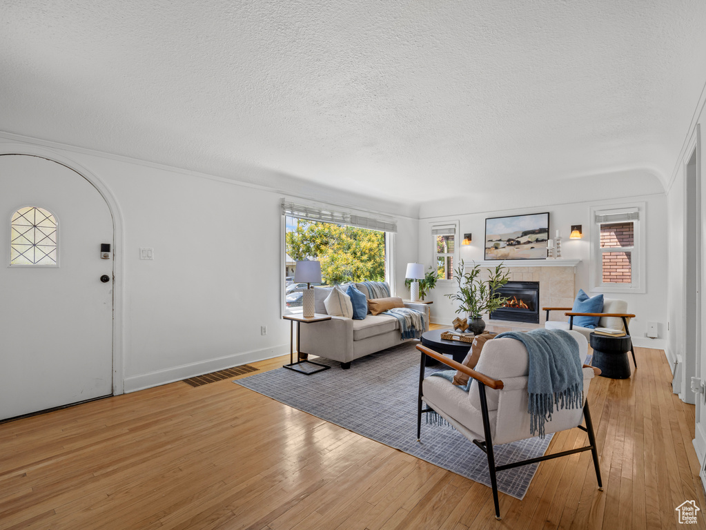 Living area with a tiled fireplace, wood-type flooring, and a textured ceiling