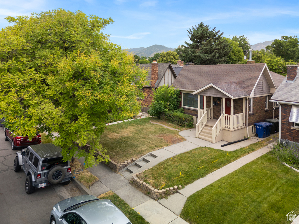 View of front of house with a chimney, a mountain view, a front yard, brick siding, and roof with shingles