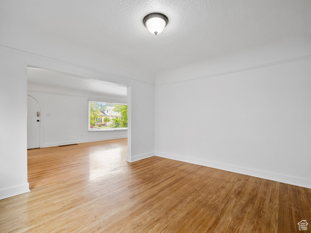 Empty room with light wood finished floors, baseboards, and a textured ceiling