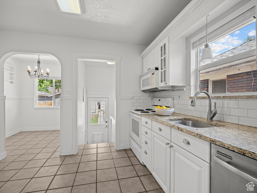 Kitchen with white appliances, light tile patterned flooring, a chandelier, decorative backsplash, and white cabinets