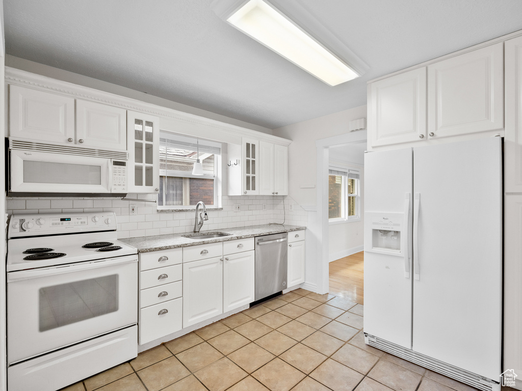 Kitchen featuring white appliances, a sink, backsplash, glass insert cabinets, and white cabinetry