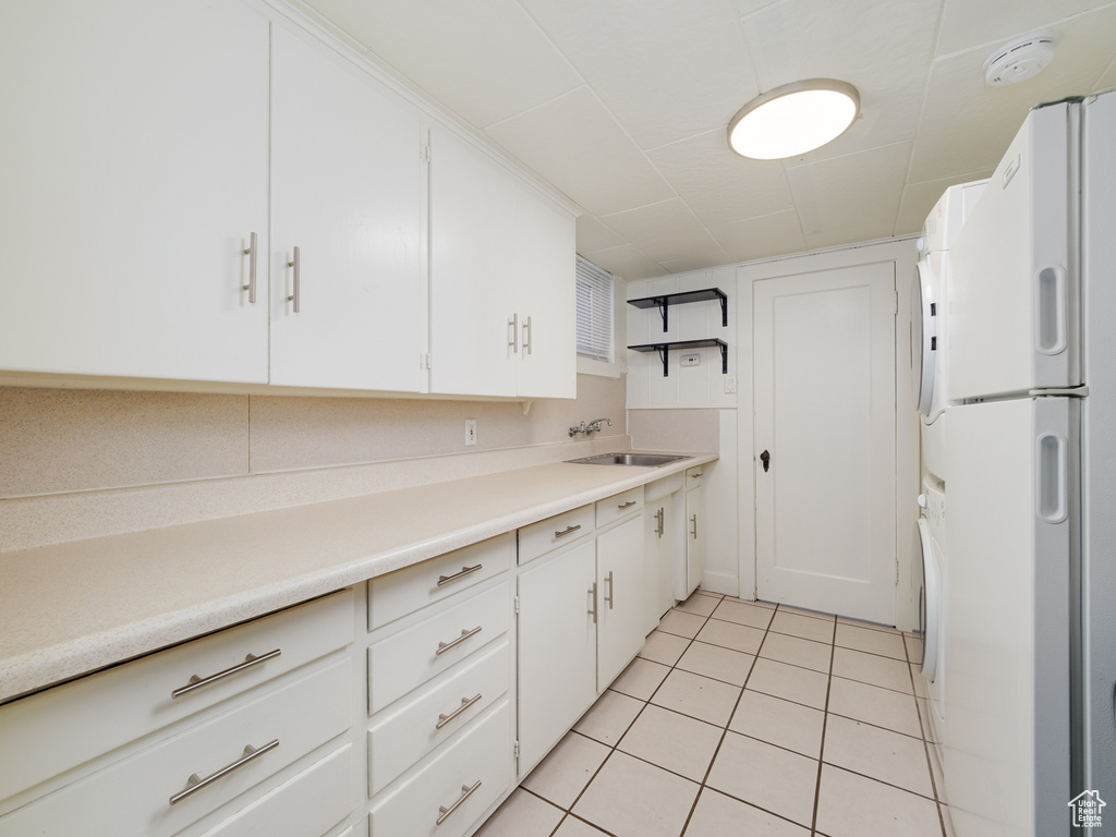 Kitchen featuring freestanding refrigerator, light tile patterned flooring, white cabinets, and stacked washing machine and dryer