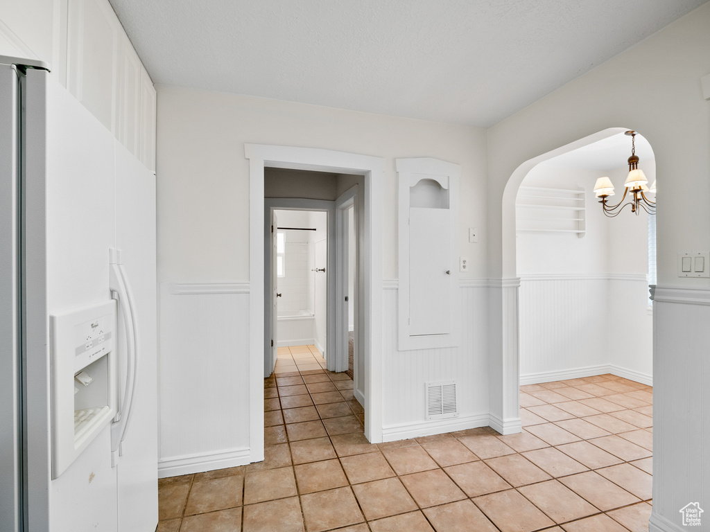 Empty room featuring light tile patterned flooring, wainscoting, a chandelier, and arched walkways