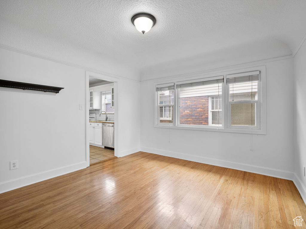 Spare room with light wood-style floors, baseboards, and a textured ceiling