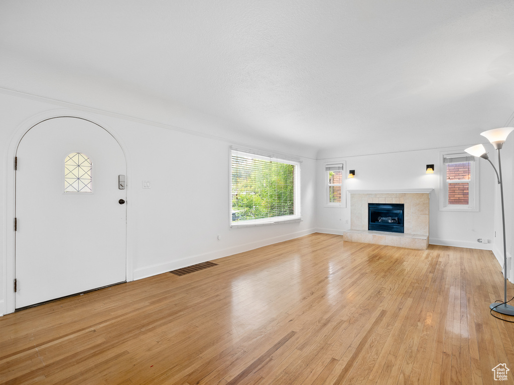 Unfurnished living room with plenty of natural light, light wood finished floors, a tile fireplace, and baseboards
