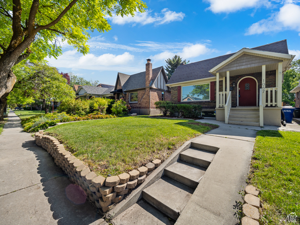 View of front of property with brick siding, a front yard, and roof with shingles