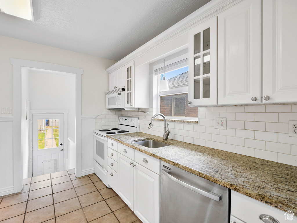 Kitchen with white appliances, a sink, white cabinets, glass insert cabinets, and backsplash