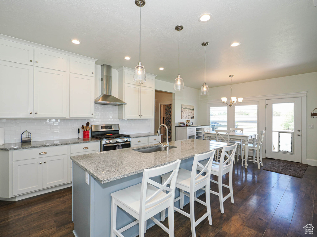 Kitchen featuring wall chimney range hood, a sink, stainless steel gas stove, decorative backsplash, and white cabinets