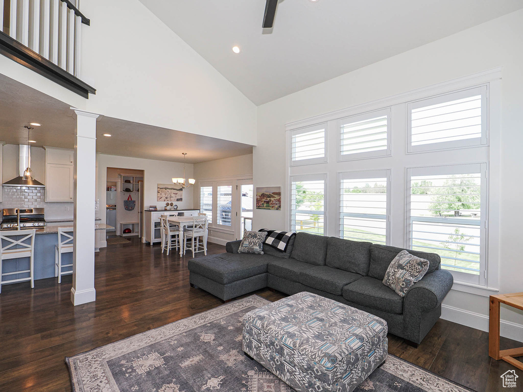 Living area with high vaulted ceiling, dark wood finished floors, decorative columns, baseboards, and a ceiling fan