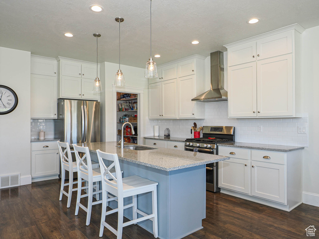 Kitchen with appliances with stainless steel finishes, wall chimney range hood, a sink, dark wood-type flooring, and white cabinetry