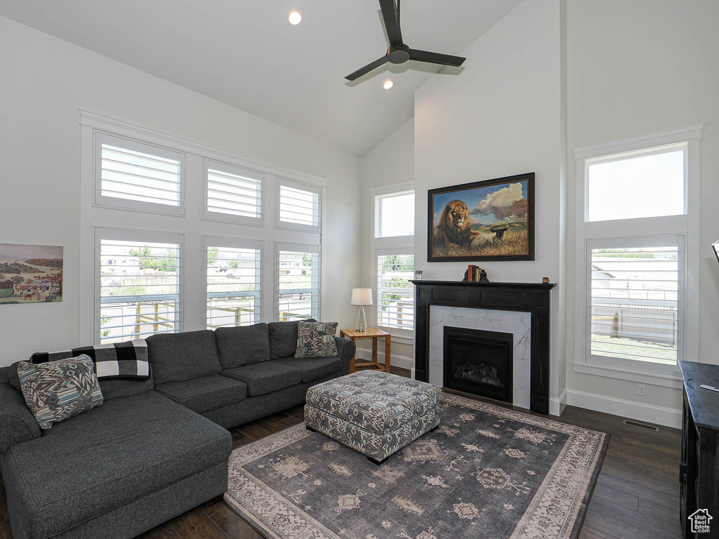 Living area featuring high vaulted ceiling, dark wood-style floors, ceiling fan, a premium fireplace, and baseboards