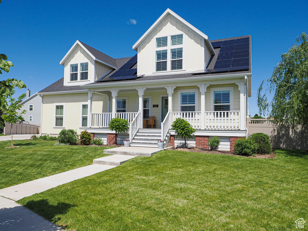 View of front facade featuring covered porch, solar panels, a shingled roof, and board and batten siding